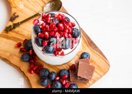 Tiramisu in ein Glas mit mascarponecreme, Blaubeeren und Granatapfel Obst, süße Tasse Dessert auf Holzbrett Stockfoto