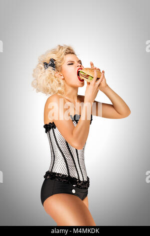 Schöne pinup Modell essen einen Hamburger auf grauem Hintergrund. Stockfoto