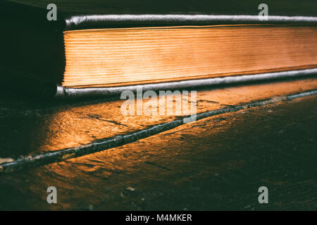 Ein geschlossenes Buch mit einem goldenen Rand auf einem alten schwarzen Holztisch mit Platz kopieren Stockfoto