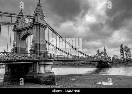 Ein schwarz-weiß Foto von Hammersmith Suspension Bridge in London über die Themse bei Ebbe Stockfoto