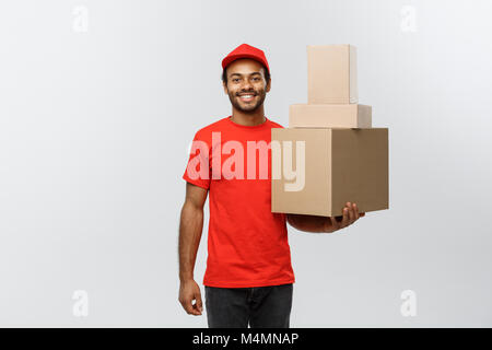 Lieferung Konzept - Portrait von Happy African American Lieferung Mann im roten Tuch Holding eine Box Paket. Auf Grau studio Hintergrund isoliert. Kopieren Sie Platz. Stockfoto