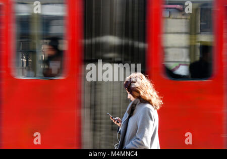 Belgrad, Serbien - Februar 17., 2018: die junge Frau auf ihrem Mobiltelefon beim Warten an der Bushaltestelle auf der Straße an einem sonnigen Wintertag mit p Stockfoto