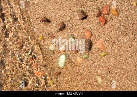 Blick nach unten an der Welle über braunen Sand und bunte Kieselsteine ein Seeufer Stockfoto