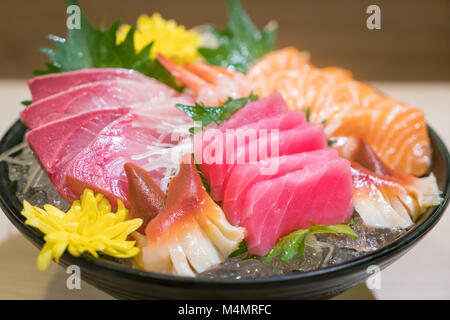 Gemischte sashimi Fisch in Scheiben geschnitten auf Eis im schwarzen Schüssel. Sashimi Lachs Thunfisch Hamachi Garnelen und Surf Ruhig, roher Fisch, japanisch Essen in asiatischen Restaurant. Stockfoto