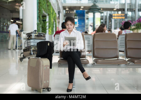 Junge Asiatin Passagier am Flughafen mit ihrem Tablet-PC während des Wartens auf ihrer Flucht im Terminal am Flughafen. Stockfoto