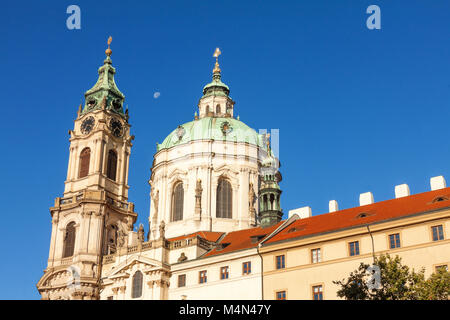 Der Uhrenturm mit der Kuppel der St. Nikolaus-Kathedrale auf der Kleinseite am frühen Morgen. Mit Halbmond auf dem Hintergrund des blauen Himmels. Stockfoto