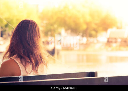 Junge Frau auf einer Bank sitzen auf der Anklagebank der Bucht bei Sonnenuntergang, Rotterdam, Niederlande Stockfoto