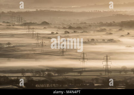 Reihe von Strommasten, die sich aus den frühen Morgen Winter Nebel in Marshwood Vale, West Dorset, England im Januar 2018. Stockfoto