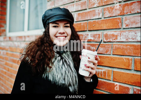 Curly mexikanische Mädchen in Leder und Plastik Tasse Kaffee zur Hand gehen an Straßen der Stadt. Stockfoto