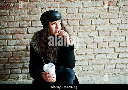 Curly mexikanische Mädchen in Leder und Plastik Tasse Kaffee zur Hand gehen an Straßen der Stadt. Stockfoto