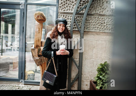 Curly mexikanische Mädchen in Leder und Plastik Tasse Kaffee zur Hand gehen an Straßen der Stadt. Stockfoto