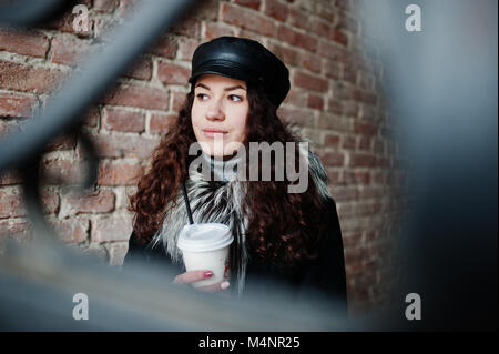 Curly mexikanische Mädchen in Leder und Plastik Tasse Kaffee zur Hand gehen an Straßen der Stadt. Stockfoto