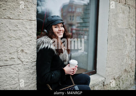 Curly mexikanische Mädchen in Leder und Plastik Tasse Kaffee zur Hand gehen an Straßen der Stadt. Stockfoto