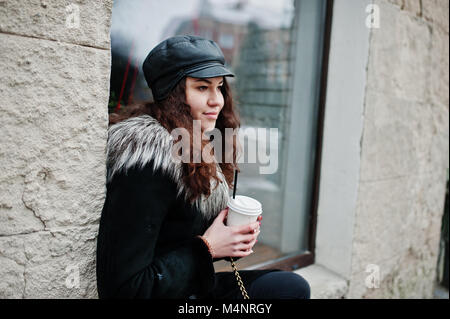 Curly mexikanische Mädchen in Leder und Plastik Tasse Kaffee zur Hand gehen an Straßen der Stadt. Stockfoto