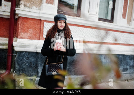 Curly mexikanische Mädchen in Leder und Plastik Tasse Kaffee zur Hand gehen an Straßen der Stadt. Stockfoto