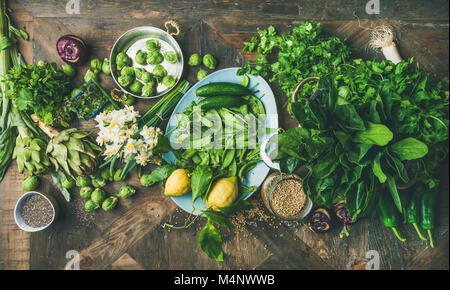 Frühjahr gesunde vegane Ernährung Zutaten zum Kochen. Flachbild-lay von Gemüse, Früchten, Samen, Sprossen, Blumen, grünen über Holz- Hintergrund, Ansicht von oben. Ernährung, Stockfoto