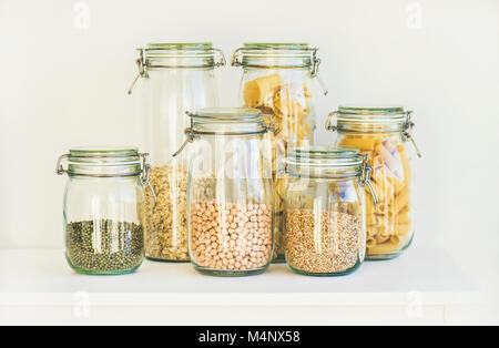 Verschiedene Rohstoffe Getreide, Körner, Bohnen und Nudeln für gesundes Kochen in Glas Vorratsgefäße auf Küche Regal, weißen Hintergrund. Sauber Essen, vegetarische, v Stockfoto