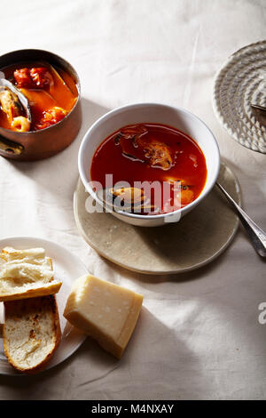 Traditionelle mediterrane Fischsuppe bouillabaisse mit Muscheln, Garnelen, Tomaten und Brühe in Kupfer Topf, und weiße Schüssel mit warmen Baguett serviert. Stockfoto