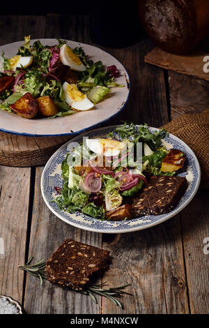 Kartoffelsalat mit Eiern, marinted Zwiebeln und Senf Dressing in zwei vintage Teller serviert. Alte hölzerne Hintergrund Stockfoto