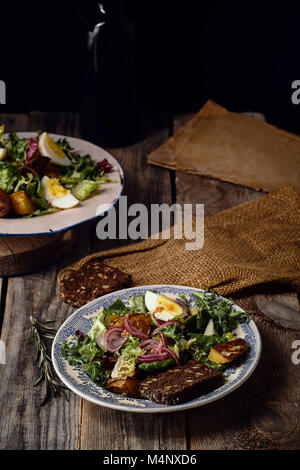 Kartoffelsalat mit Eiern, marinted Zwiebeln und Senf Dressing in zwei vintage Teller serviert. Alte hölzerne Hintergrund Stockfoto