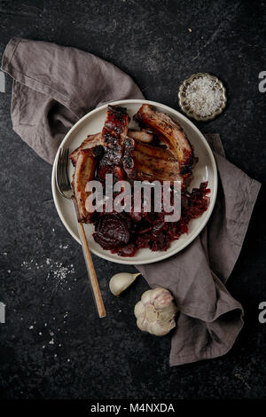 Hauptgericht mit gegrillten Schweinerippchen in dicken barbeque Sauce garniert mit Rotkohl und Rüben Geschmortes in Rotweinsauce. Dunkel strukturierten Hintergrund Stockfoto