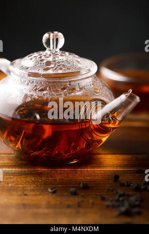 Transparentes Glas Teekanne mit heißem schwarzem Tee auf hölzernen Tisch. Vertikale Nahaufnahme. Stockfoto