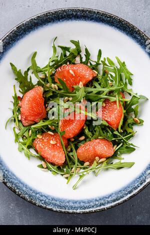 Rucola Salat mit Grapefruit und Sonnenblumenkerne auf grauem Beton Hintergrund close-up Stockfoto