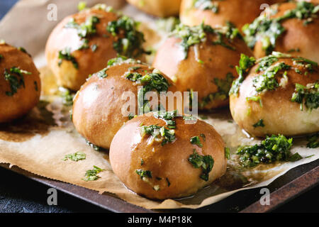 Traditionelle ukrainische hausgemachter Knoblauch Brötchen pampushki für borschtsch Suppe mit Öl und Koriander auf alten Backblech mit Backpapier über Dunkelblau Textur Stockfoto