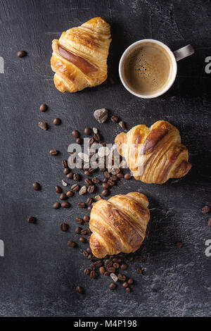 Frisch gebackene Croissants und traditionelle Tasse Espresso Kaffee, Kaffeebohnen, Zucker über schwarzen Textur Hintergrund. Ansicht von oben, kopieren Raum Stockfoto