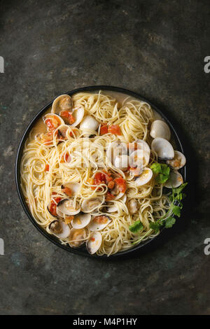 Pasta Spaghetti Vongole in Tomaten-Sahne-Sauce in schwarz Platte über alte Metall Textur Hintergrund. Ansicht von oben, Raum Stockfoto