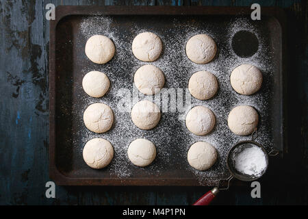 Hausgemachte almond Cookies mit Zucker Pulver, mit Vintage Sieb, die auf alten Backofen Fach über Dunkelblau Holztisch. Dunklen rustikalen Stil. Ansicht von oben, Raum Stockfoto