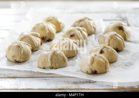 Raw ungebackene Gebäck. Bereit, hausgemachte Ostern traditionelle Hot Cross Buns auf Backpapier über weiße Holztisch mit Fenster im Hintergrund zu backen. Natürliche Stockfoto