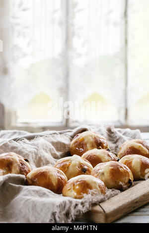 Hausgemachte Ostern traditionelle Hot Cross Buns auf Holz- Fach mit textilen über weiße Holztisch. Im Hintergrund angezeigt. Tageslicht. Im rustikalen Stil. Stockfoto