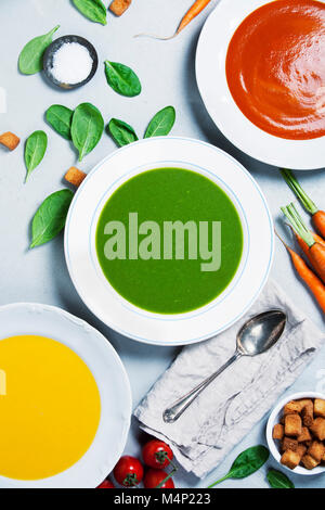 Kürbis, Tomaten und Spinat Suppen über grauer Beton Hintergrund, Ansicht von oben. Sauber Essen, Diäten, vegan, Vegetarisch, gesunde Ernährung Konzept Stockfoto