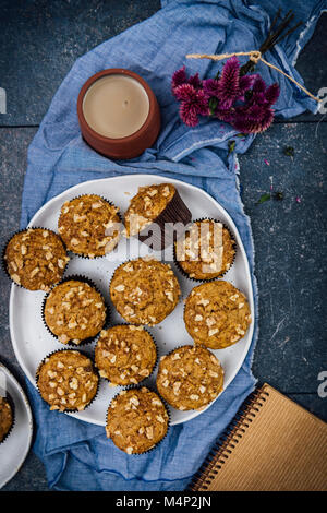 Banane nuss Muffins serviert auf einem großen weißen Keramik Platte von der Ansicht von oben fotografiert. Eine Tasse Kaffee, Blumen, ein Notebook zu begleiten. Stockfoto