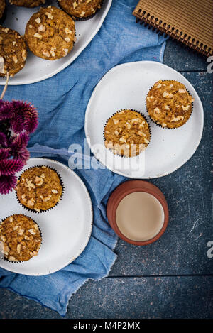 Banane nuss Muffins serviert auf zwei weiße keramische Platten von der Ansicht von oben fotografiert. Eine Tasse Kaffee, Blumen, ein Notebook zu begleiten. Stockfoto