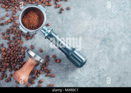 Portafilter mit gemahlenen Kaffee, Sabotage- und Kaffeebohnen auf einen konkreten Hintergrund mit kopieren. Barista Konzept von oben. Stockfoto