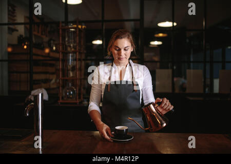 Coffee shop besitzer Kaffee in eine Schale giessen. Porträt einer Frau, die sich in einem Coffee Shop. Stockfoto