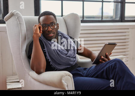Die schwarze afrikanische amerikanische Student sitzt auf einem Stuhl und mit einem Tablet-PC. Stockfoto