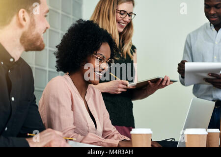 Lächelnd afrikanischen Geschäftsfrau, umgeben von einer vielfältigen Gruppe von Kolleginnen und Kollegen beim zusammen in einem modernen Büro arbeiten Stockfoto