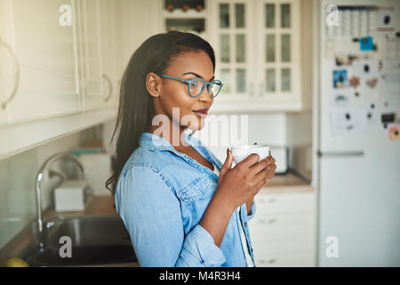 Junge afrikanische Frau tief in Gedanken, während allein in ihrer Küche zu Hause trinken eine Tasse frischen Kaffee Stockfoto