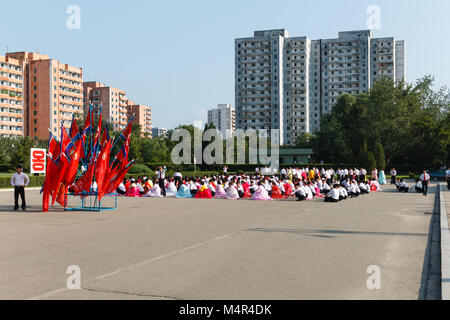 Pyongyang, Nordkorea - Juli 27, 2014: Koreanische Männer und Frauen sitzen auf dem Platz in Erwartung auf den Beginn der Masse tanzt zu den da gewidmet Stockfoto