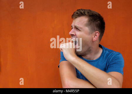 Der junge Mann gähnt mit Müdigkeit, über seinen Mund mit seiner Hand. Er ist gelangweilt. Stockfoto