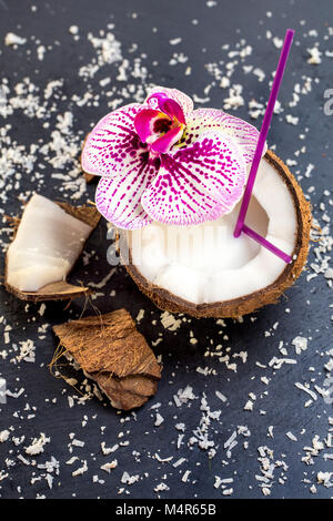 Kokosnüsse mit Kokosnüssen Flocken und Orchidee am grauen Stein hinterg Stockfoto