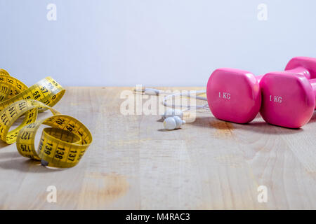 Stil leben mit rosa Gewichte, Ohrhörer und ein gelbes Band measrument. Fitness. Konzept Stockfoto