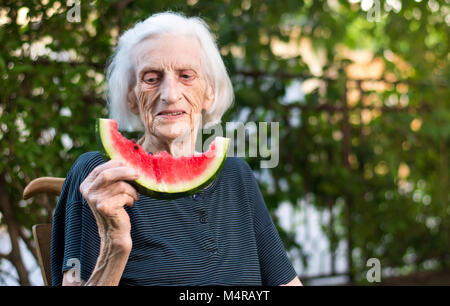 Ältere Frau Essen Wassermelone Frucht im Hinterhof Stockfoto