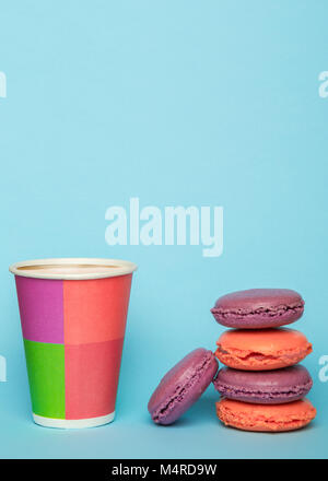 Französische macarons und Pappbecher mit Latte auf dem blauen pastellfarbenen Hintergrund. Einfaches Frühstück mit Makronen. Stockfoto