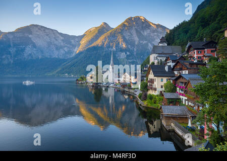 Klassische Postkarte Blick auf berühmte Hallstatt Stadt am See in den Alpen mit traditionellen Fahrgastschiff am frühen Morgen Licht in der Dämmerung auf einem schönen Sunn Stockfoto