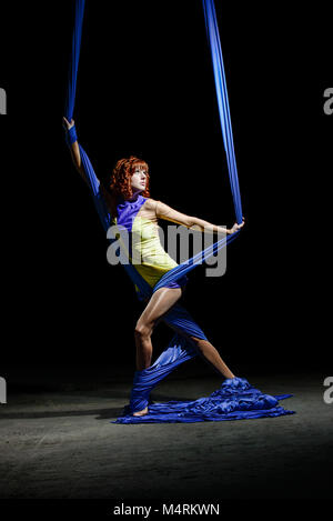 Schöne junge sportliche Mädchen, mit redhead in gelb Kostüm, mit wunderschönen blauen Antenne Seide auf das Licht in der Dunkelheit posieren. Stockfoto