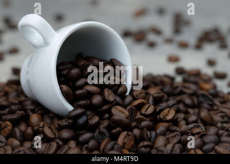 Close Up - Kaffee Bohnen verschüttete aus weißer Keramik Schale, geröstete Kaffeebohnen als Hintergrund der Komposition. Stockfoto